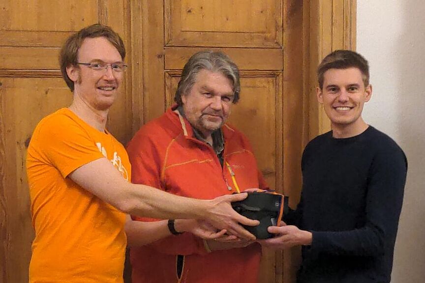 Drei Männer, von denen einer ein Geschenk überreicht bekommt.