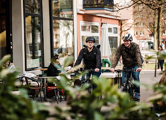 Radfahrer mit Helm Zwei Männer mit Helm fahren auf einem Radweg im urbanen Raum